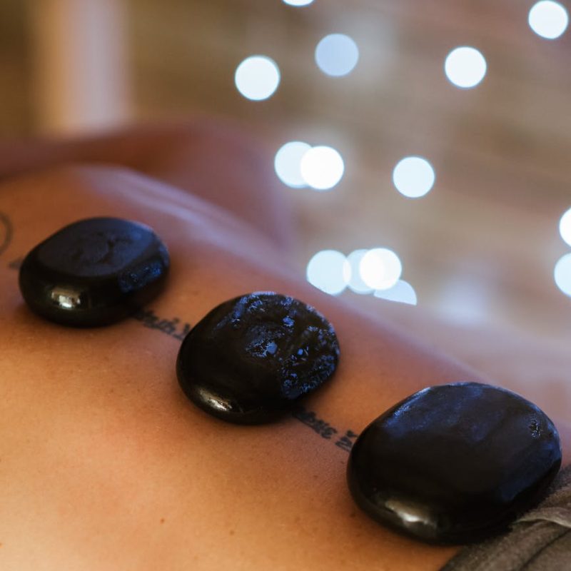 crop person with hot stones on back during massage procedure